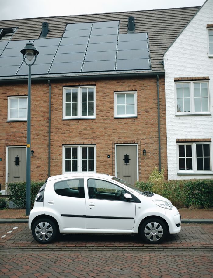 A white car parked in front of modern townhouses with solar panels in Hoofddorp, Netherlands.